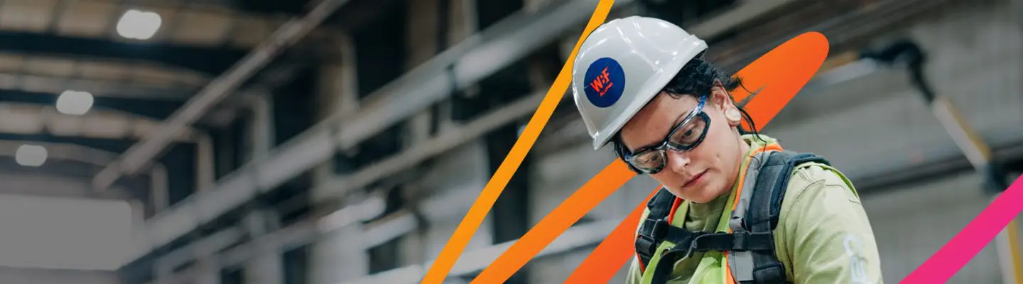 A woman wearing a PPE (hard hat and safety glasses) working with tools