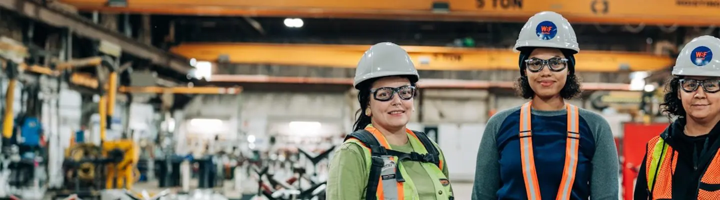 Image of three women wearing construction gear standing in workshop