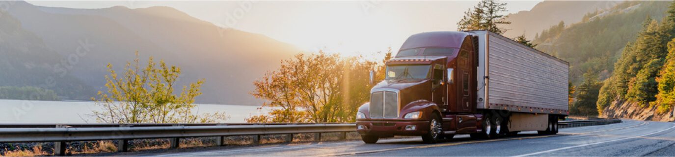 Photo of transport truck driving on a highway near a mountain lake.